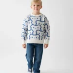 سويت شيرت أولادي شتوي كنزة محبوكة باللون الأبيض مائل للبيج. يتميز بنقوش زرقاء على شكل وجوه.